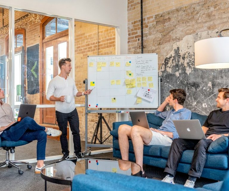 Besprechung in modernem Raum mit Präsentation und vier Personen am Tisch.