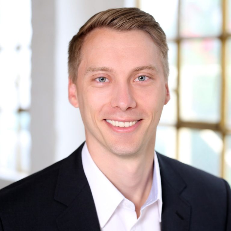 Porträt des Geschäftsführers und Gründer in einem Anzug mit hellem Hintergrund.