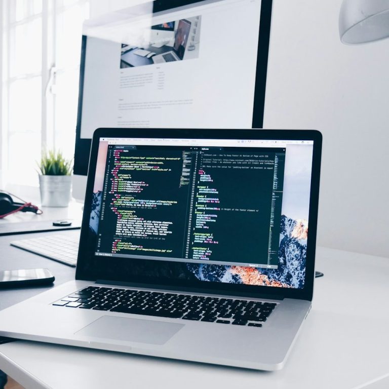 Laptop mit Codezeilen auf dem Bildschirm, daneben Smartphone und Pflanze auf einem Tisch.